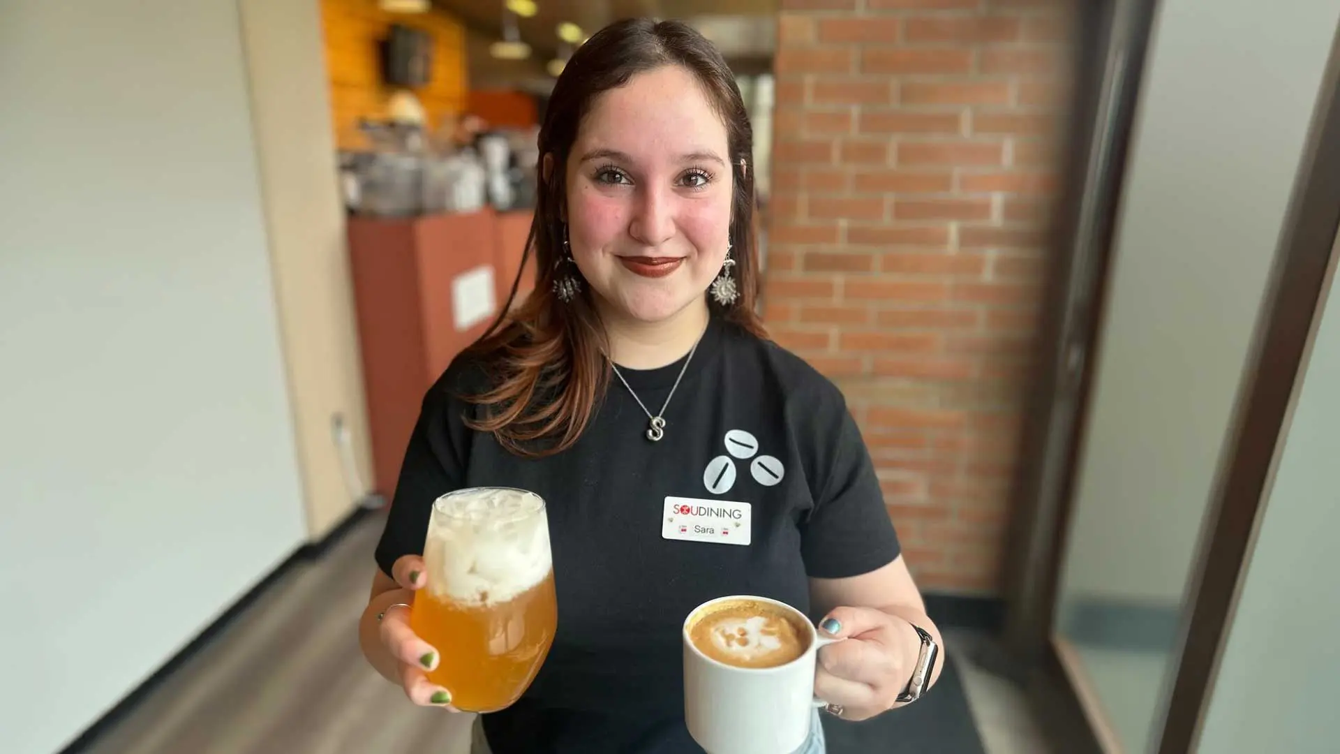 Employee holding an ice beverage and a latte while smiling
