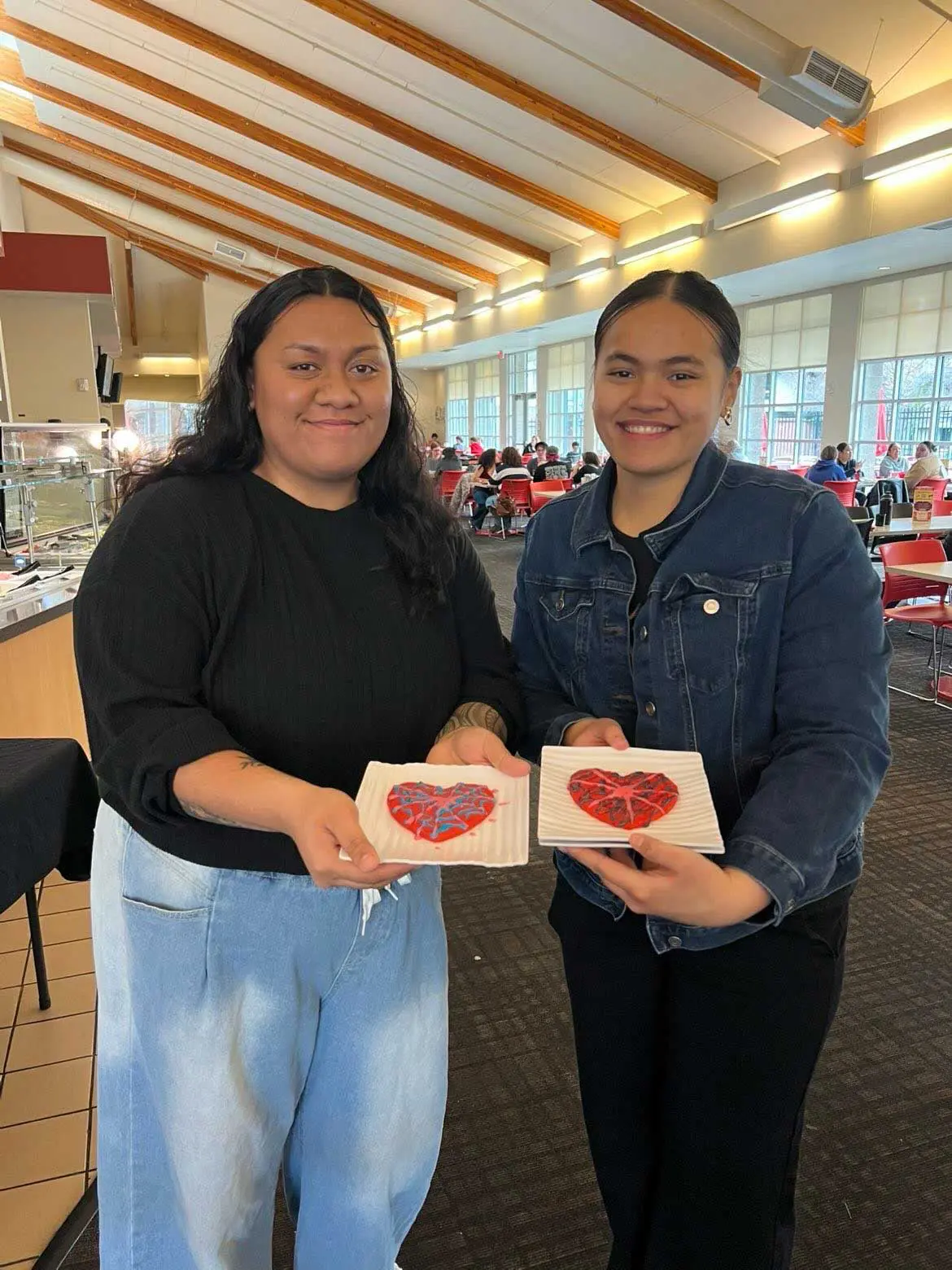Two students holding up heart shaped cookies they decorated