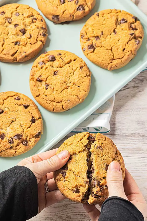 Hands breaking chocolate chip cookies in half with cookies in a box in the background